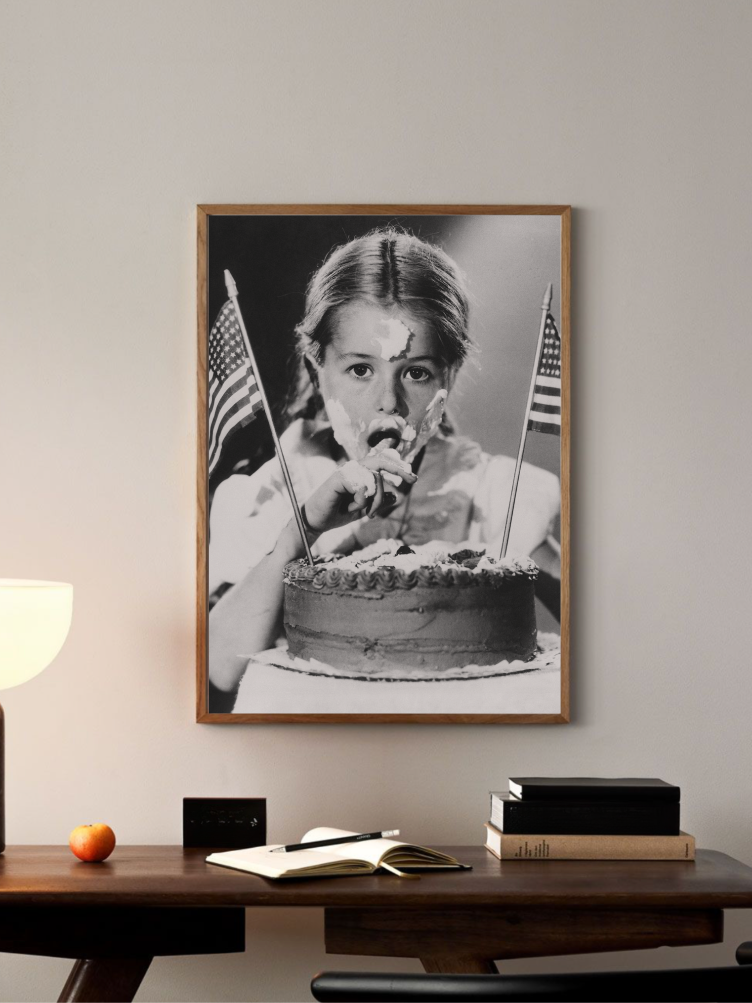 Framed black and white poster of a girl eating a cake with American flags on a wall above a desk.