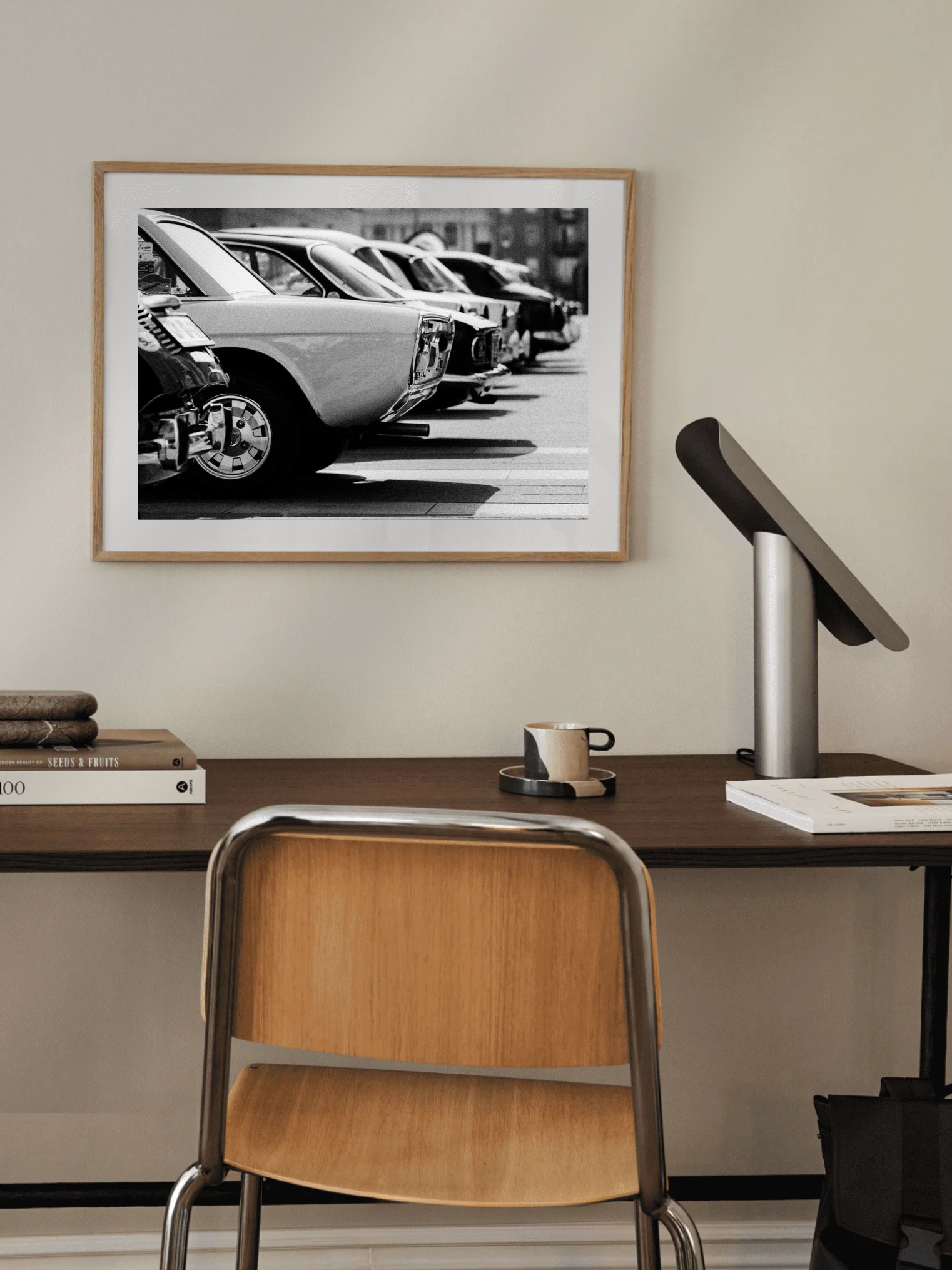 Framed black and white photograph of vintage classic cars on a wall above a desk with a chair.