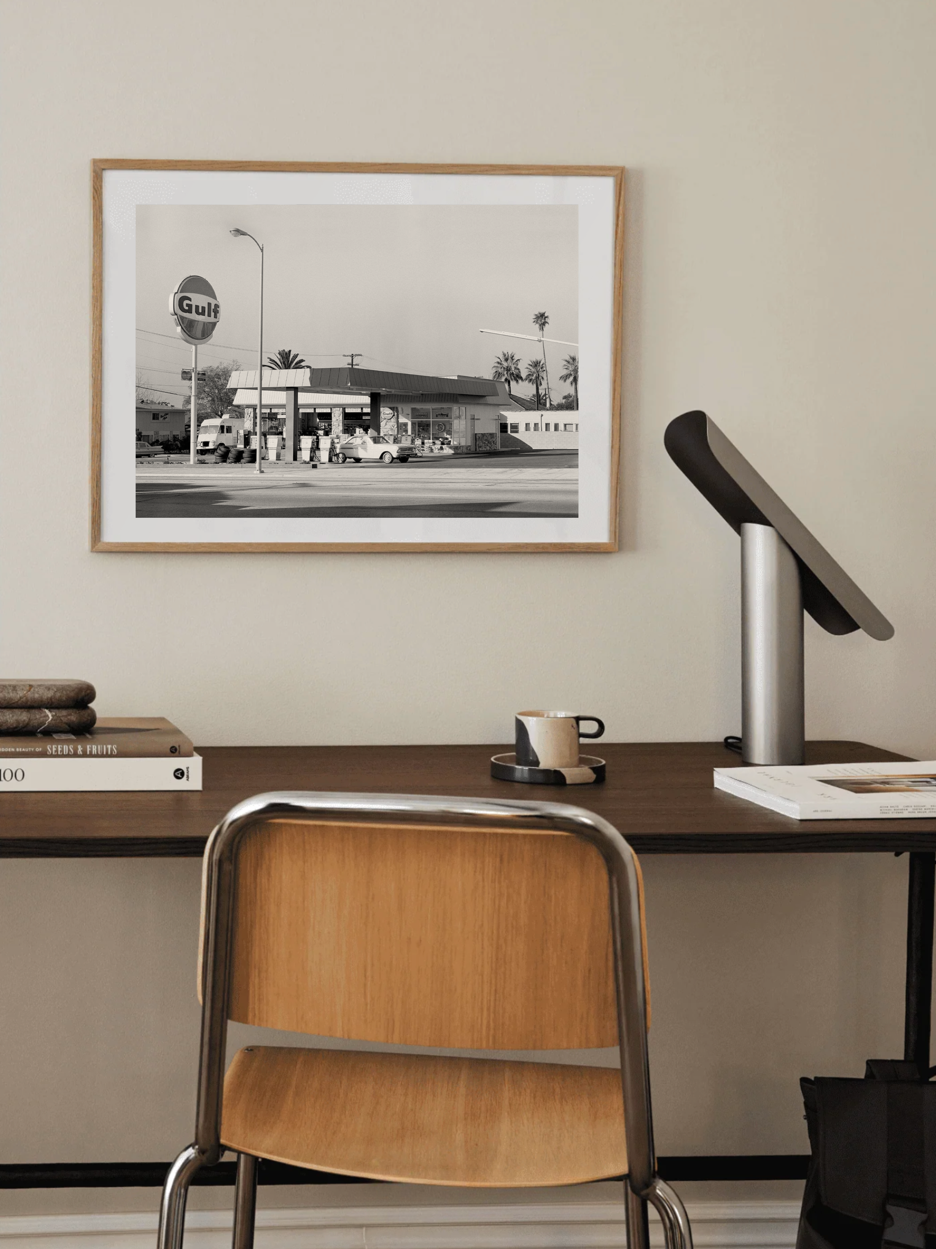 Framed Black and white photo of an old-fashioned gas station on a wall above a desk with a chair.