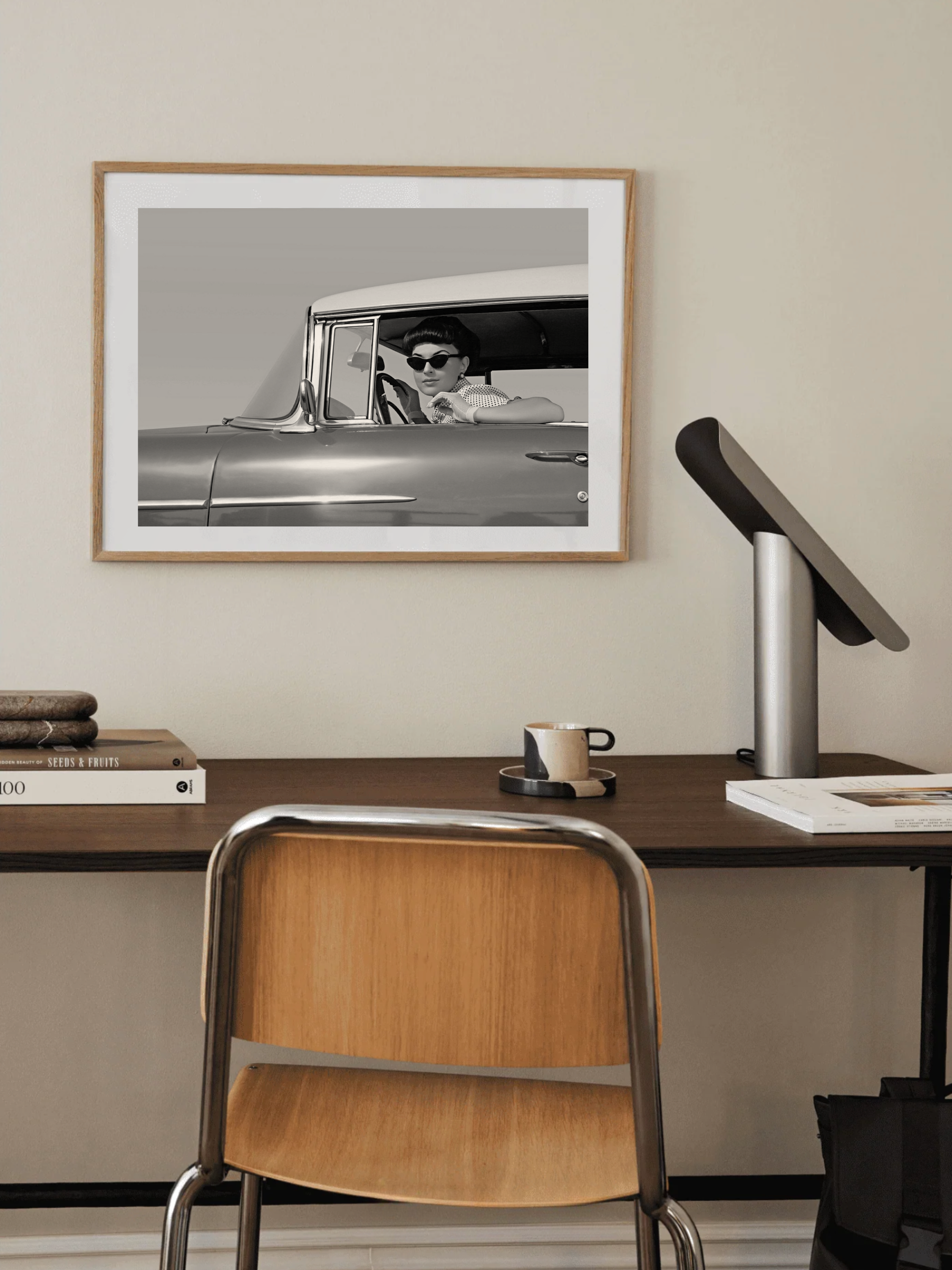 Framed Fashion photography wall art in black and white of a woman  in a vintage car on a wall above a desk with a chair.