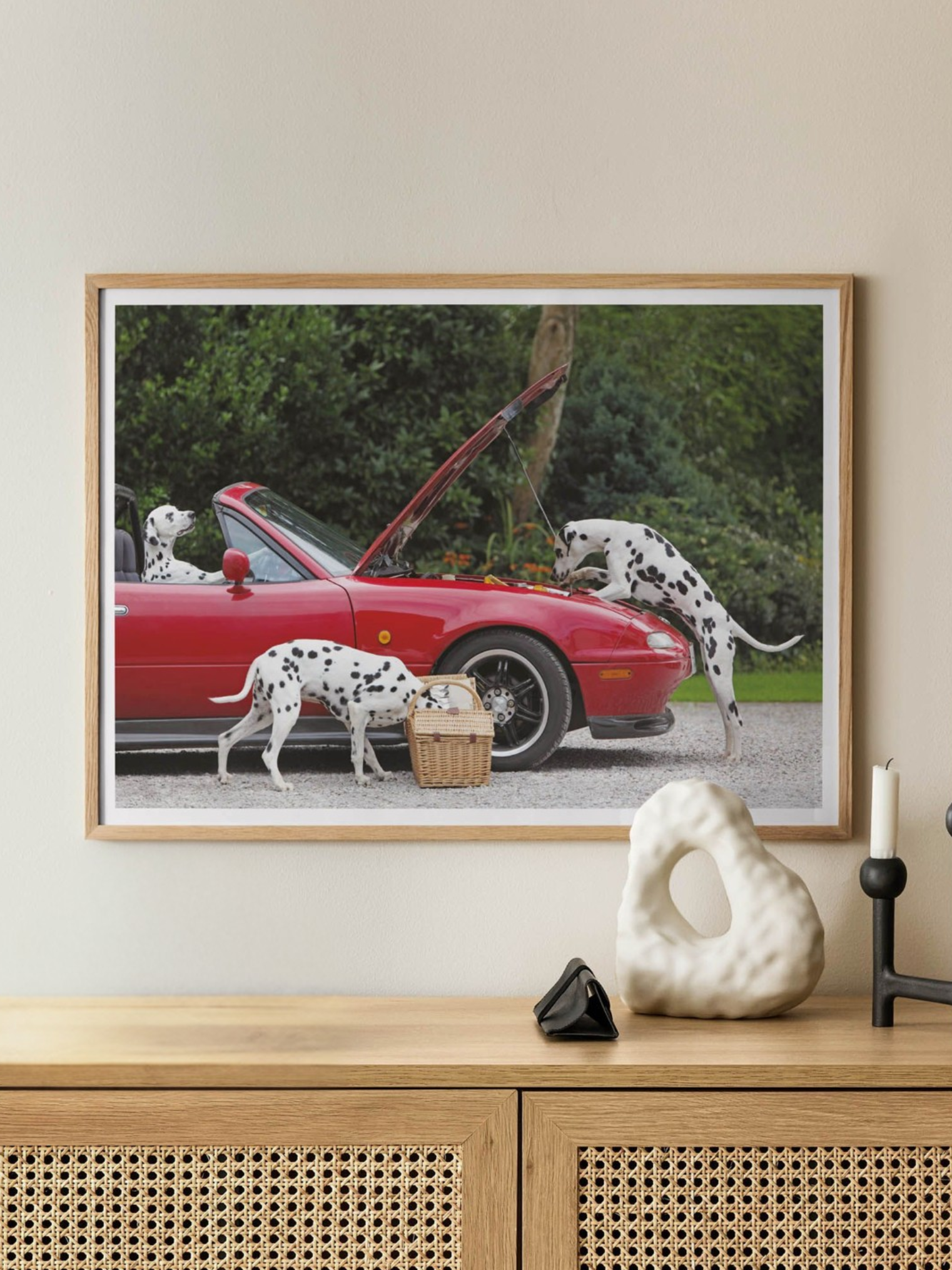 Framed artwork of three Dalmatian dogs by a red car on a wall above a wooden console table.