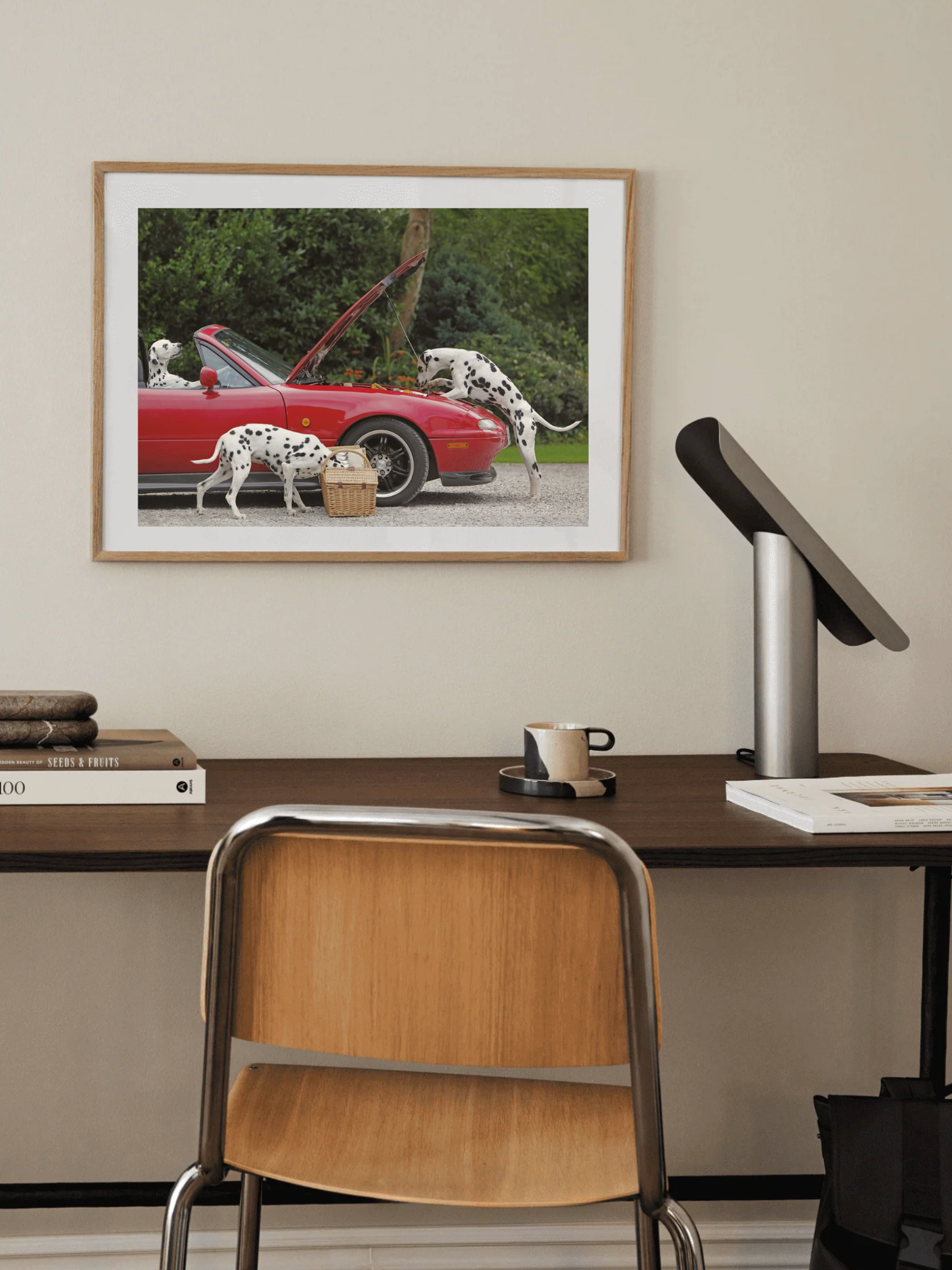 Framed photograph of a red convertible car with dalmatians on a wall above a desk.
