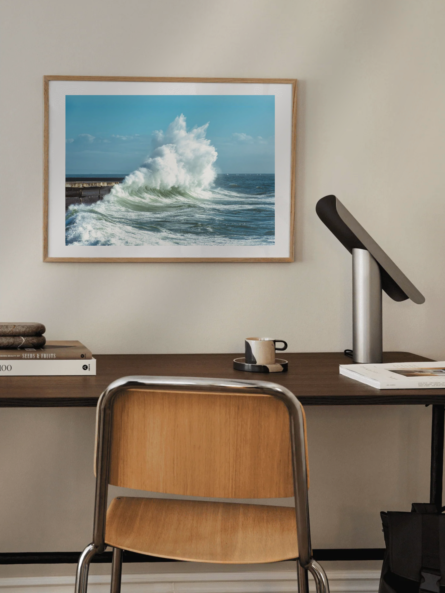 Framed artwork of a wave over a desk with a chair and lamp.