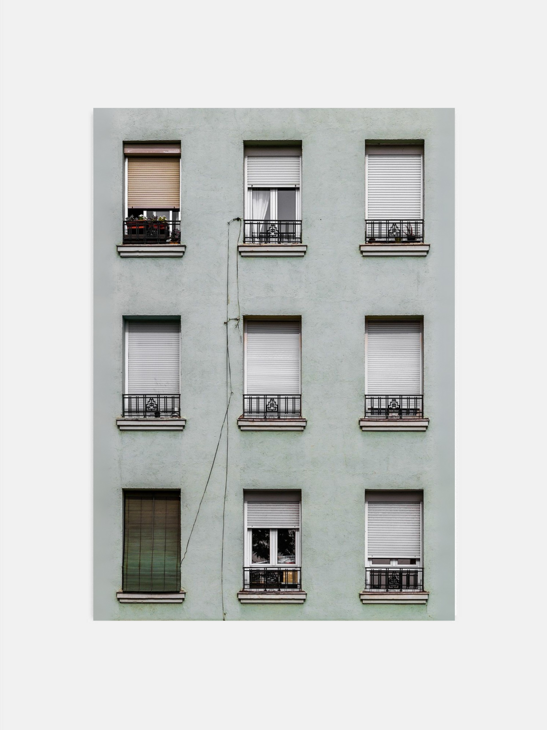 Light green building facade with symmetrically arranged windows featuring various window coverings.