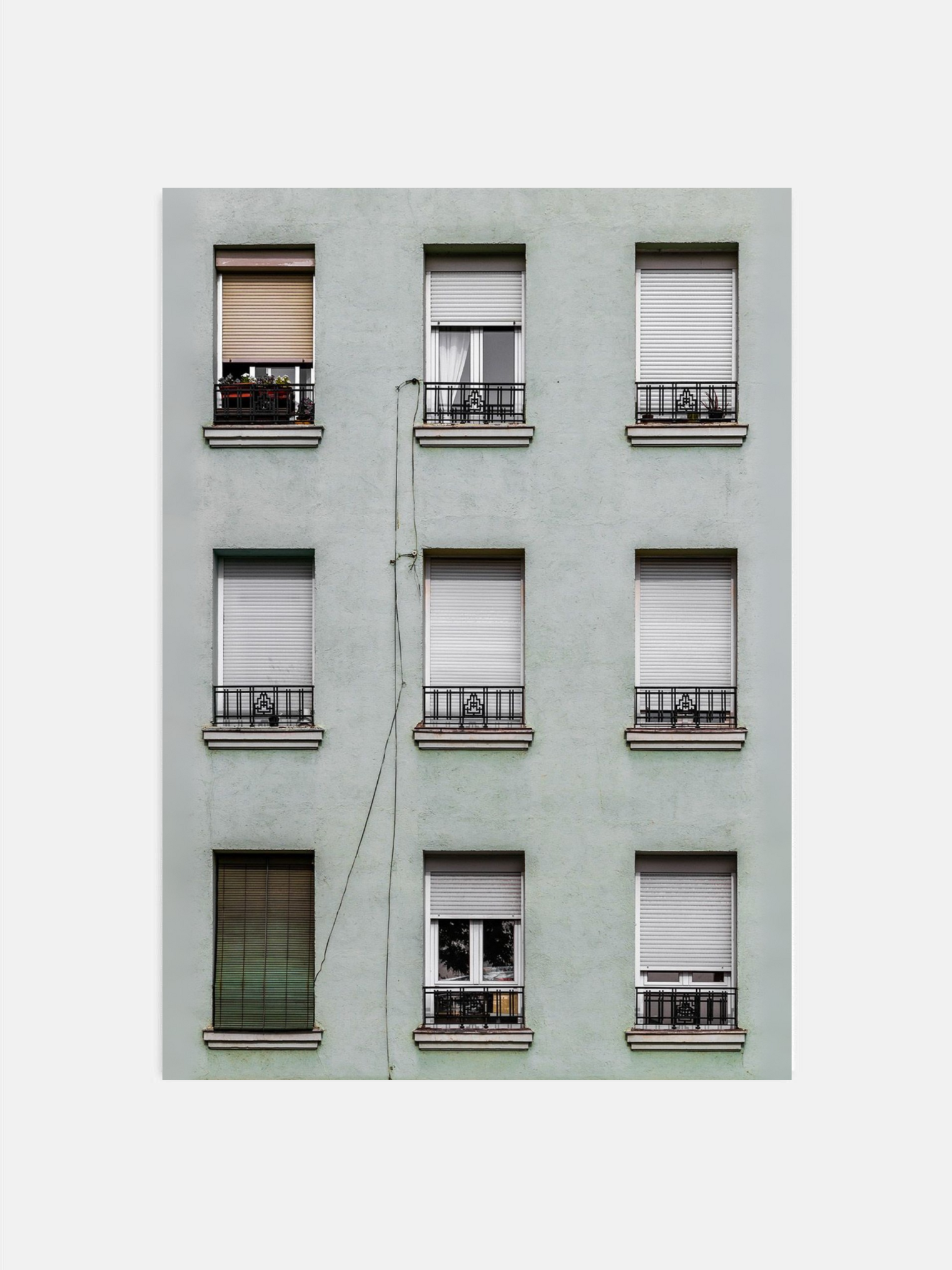 Light green building facade with symmetrically arranged windows featuring various window coverings.