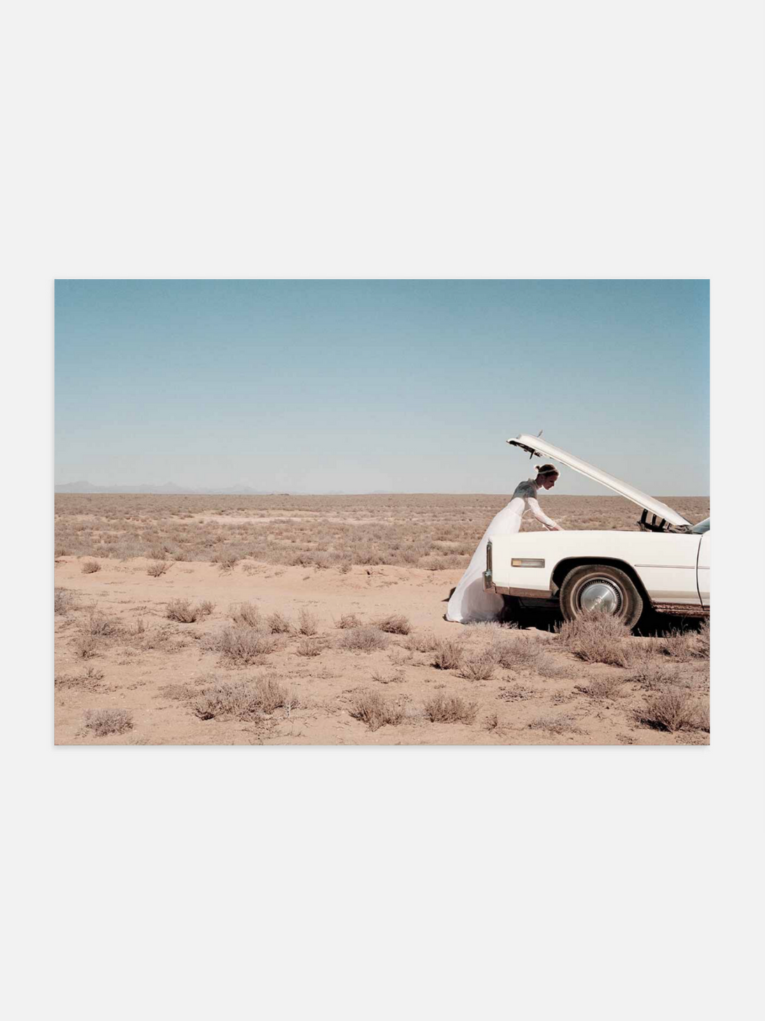 Bride in white dress beside broken-down car in desert